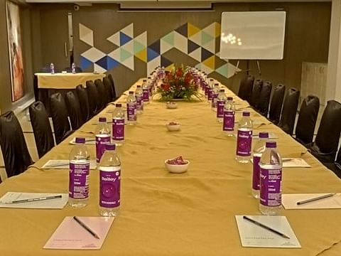 A long conference table set up for a meeting. There are water bottles, notepads, and pens arranged neatly at each seat. A whiteboard stands in the background, and the walls are decorated with a geometric pattern.